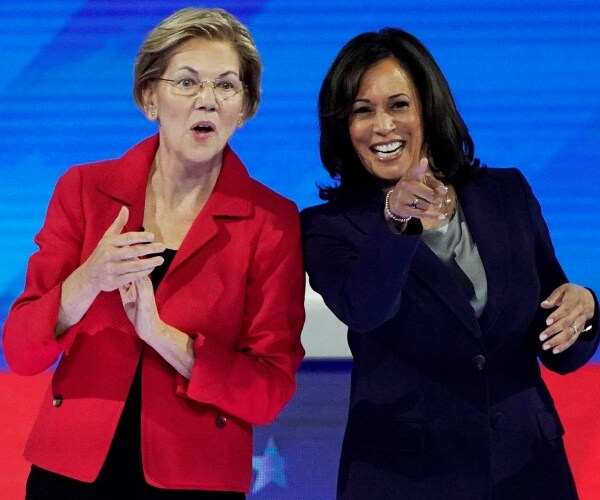 warren in a bright red blazer and kamala harris in a blue pantsuit point and smile at the audience in the debate