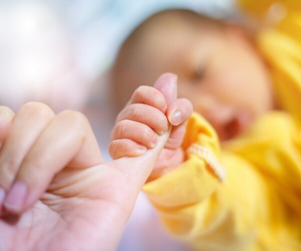newborn baby in a yellow outfit holding a woman's pinky finger