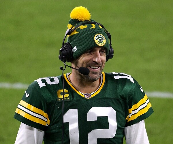 aaron rodgers stands on football field sideline wearing headset