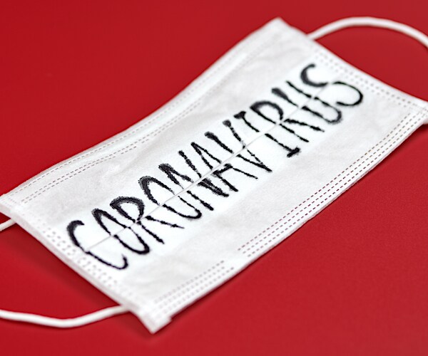 a face mask with conoravirus etched on it lays on a red table