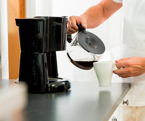 man pouring coffee from carafe from coffee machine