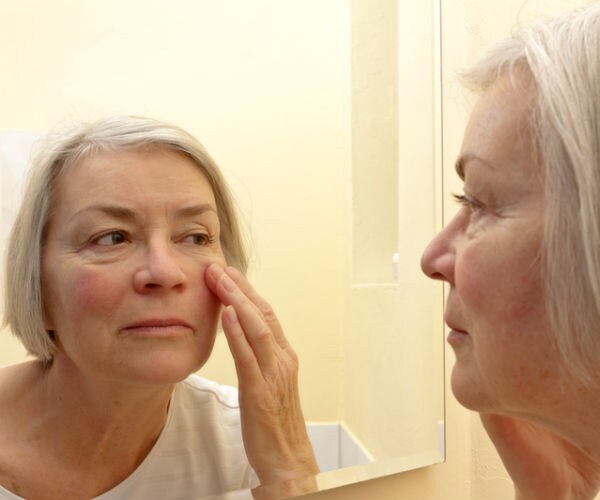 older woman looking at her complexion in the mirror