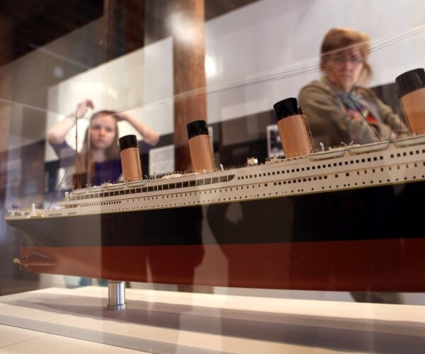 people look inside a glass case with a model of the titanic ship inside it