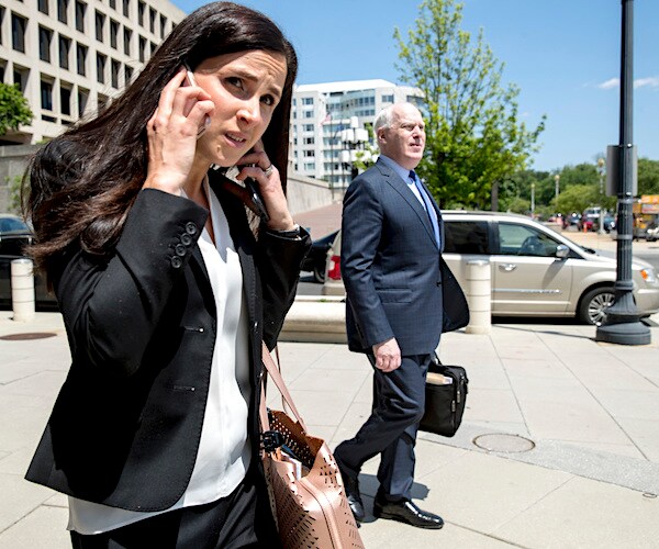 a woman wearing black holds a phone to her ear and while a man in the background walks briskly to dodge cameras