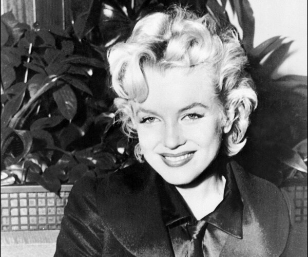 monroe in a dark coat smiling with leaves behind her