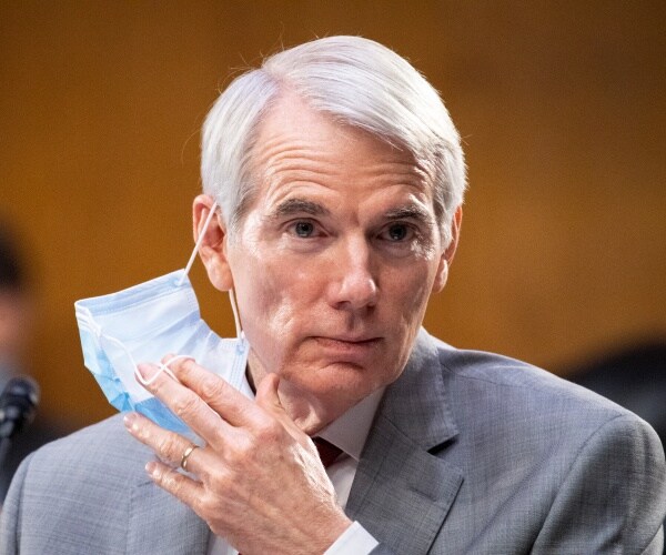 portman in a light gray suit taking off his face mask