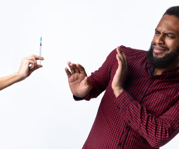 man with hands up, afraid, as healthcare worker holds needle up to him