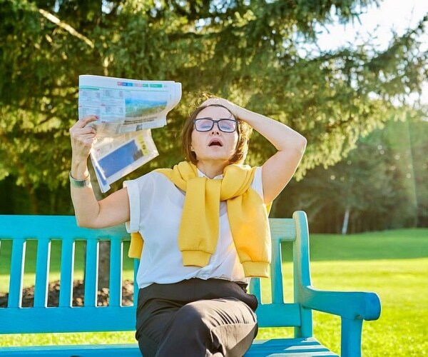 woman having a hot flash while sitting on a bench in the park