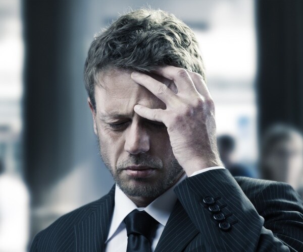 man in suit with hand up to head, suffering headache