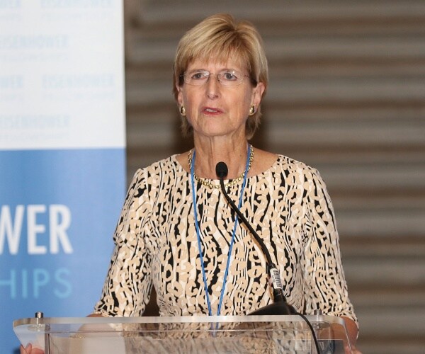whitman in a tan black and white patterned dress speaking at a podium