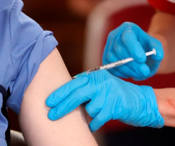 nurse with blue gloves gives a patient a shot of the covid vaccine
