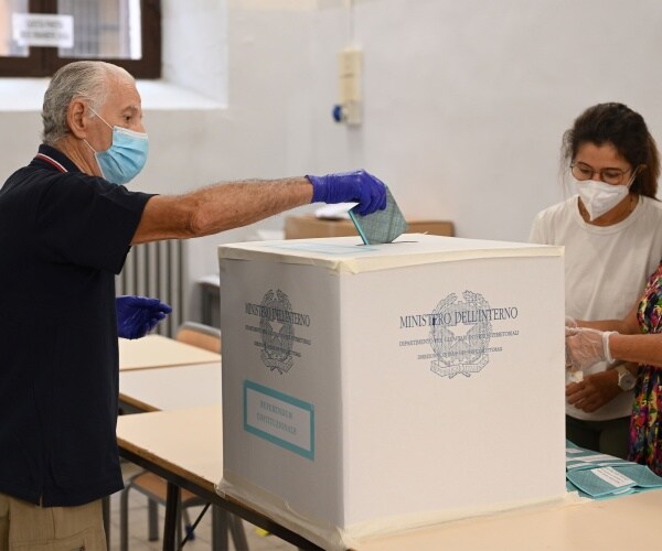 man puts his ballot in a box with election workers nearby