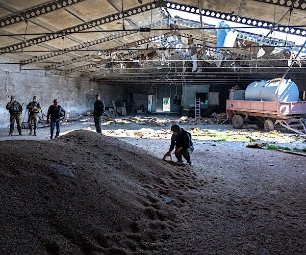 Local government officials and Ukrainian soldiers inspect a wheat grain warehouse earlier shelled by Russian forces