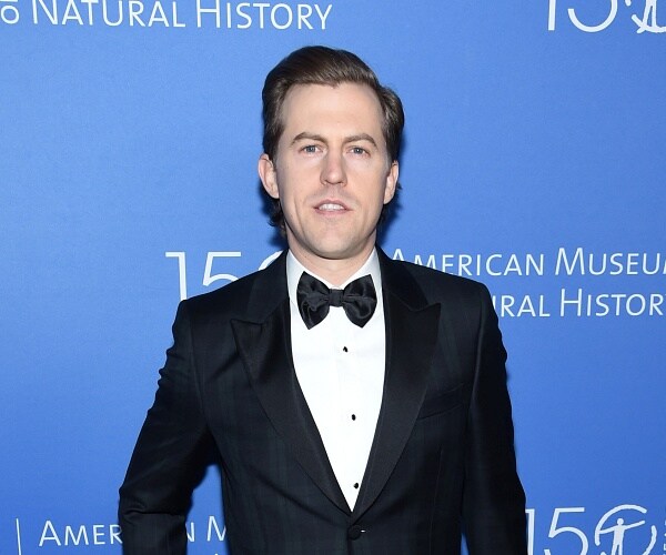 alex moffat stands on red carpet