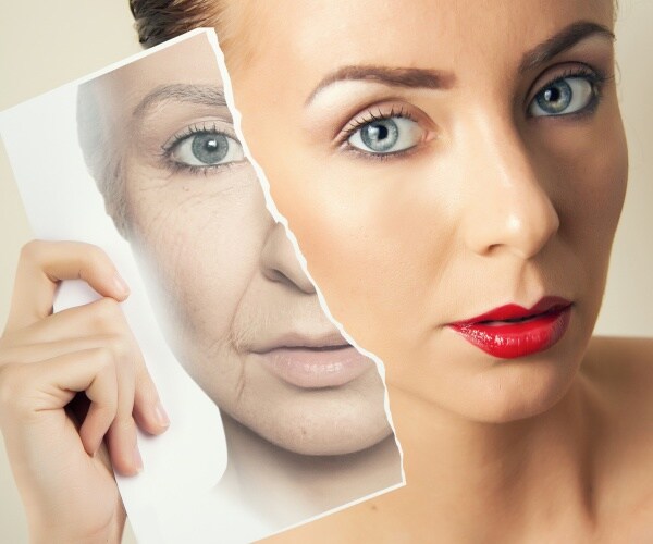 woman wearing red lipstick holding a picture of an aging face with sagging skin