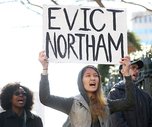 a protestor holds a sign that reads evict northam outside the governor's residence in virginia