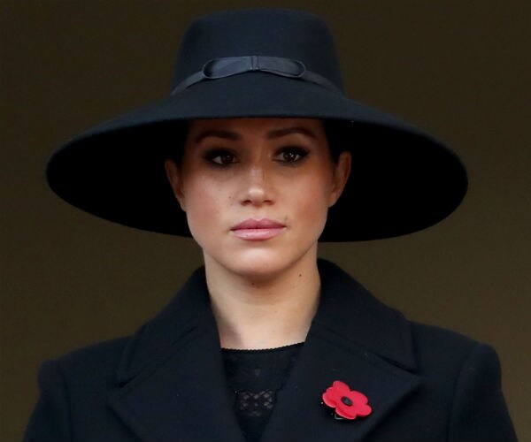 Meghan, Duchess of Sussex is dressed in all black with a red flower on her lapel.
