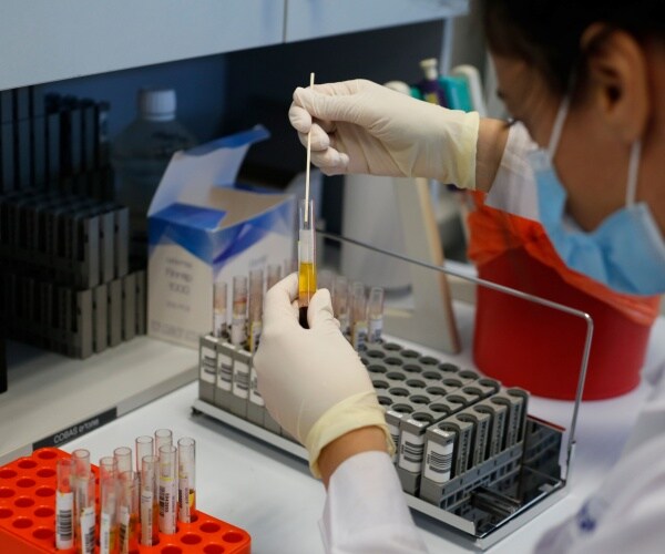 woman wearing a face mask puts a metal tool inside a test tube containing a blood sample
