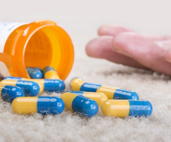 vial of drugs on carpet, close up of hand of someone who just overdosed next to it