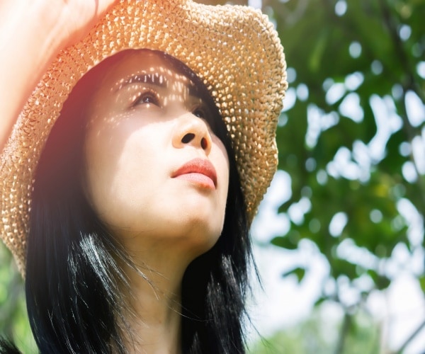 woman with contemplative expression out in sun with hat on
