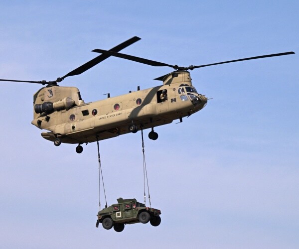 a tandem rotor helicopter transports a military vehicle by airlift