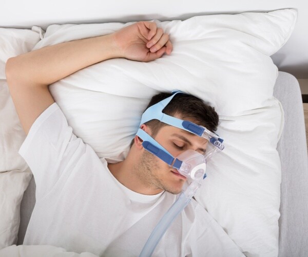 man asleep in bed with cpap machine mask on 