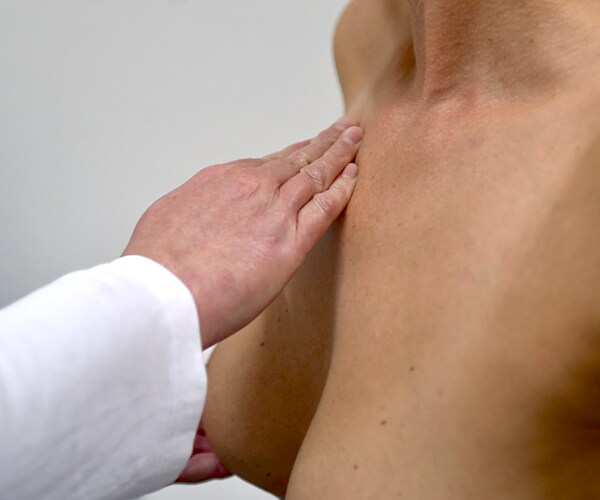 a doctor's right arm examines the bare chest of a woman in a routine breast cancer screening