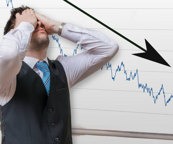 a man puts his hands to his face in disgust while standing inf front of a chart showing a downward spike