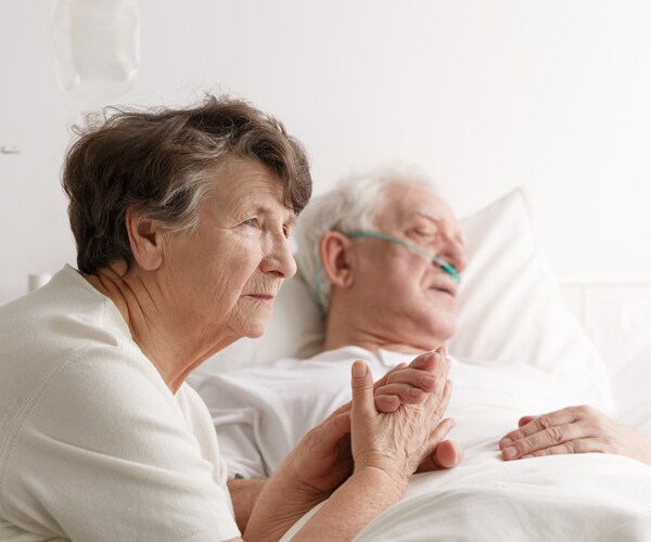 an elderly woman comforting a sick man in a hospital bed