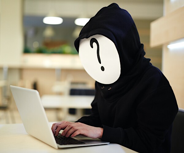 a man with a question mark on a piece of paper covering his face is typing on a laptop computer