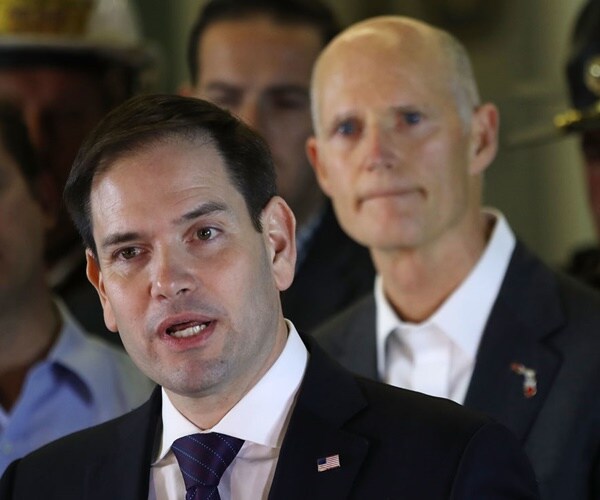 marco rubio speaks with rick scott standing behind him