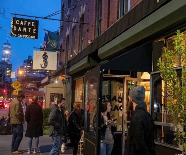 people form a line at caffe dante bar and restaurant with high rise buildings in the background