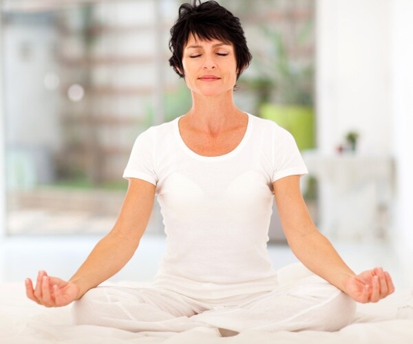 woman wearing all white sitting on floor, legs crossed, meditating