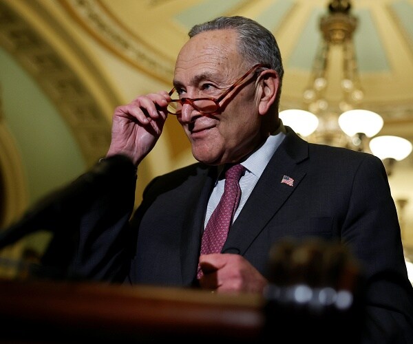 chuck schumer stands behind podium and looks over glasses