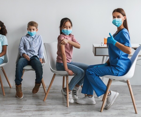 healthcare worker giving children the covid vaccine gives thumbs up