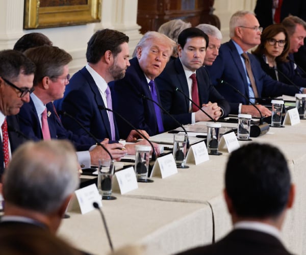 donald trump talks with people seated on both sides of him at a table