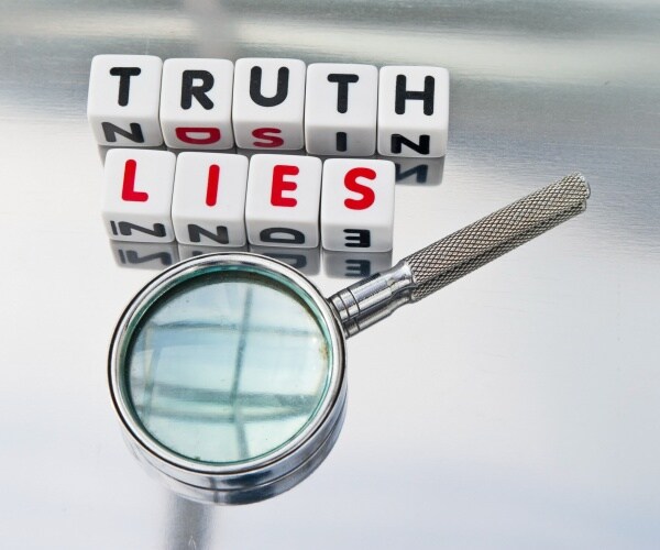 truth and lies inscribed in uppercase letters on small white cubes in black and red colors with hand magnifier
