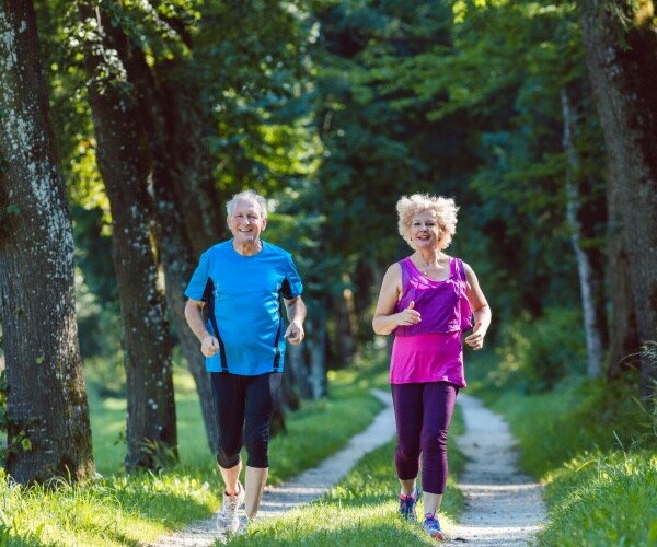 older man and woman smiling while running on a trail