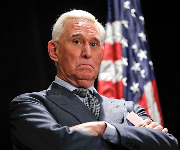 roger stone crosses his arms in front of the american flag