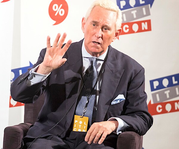 roger stone holds up five fingers of his right hand while making a point during politicon