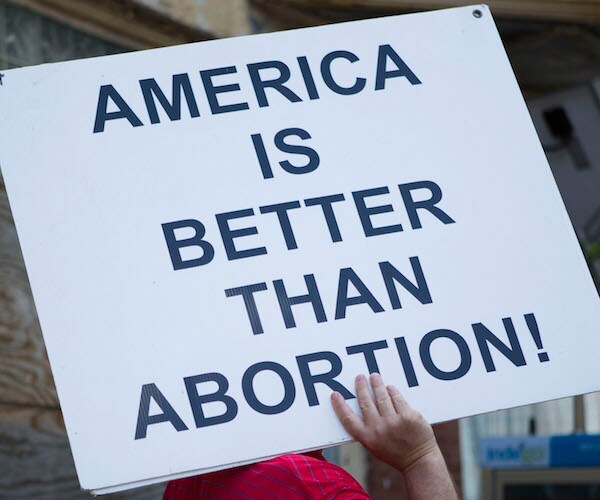 a pro life protestor holds up a sign reading american is better than abortion