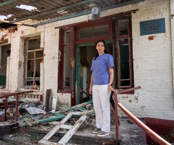 a woman stands outside a broken building