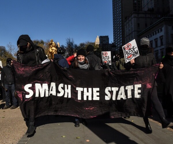 antifa activists dressed in black hold up a banner saying "smash the state" and hold signs protesting an event