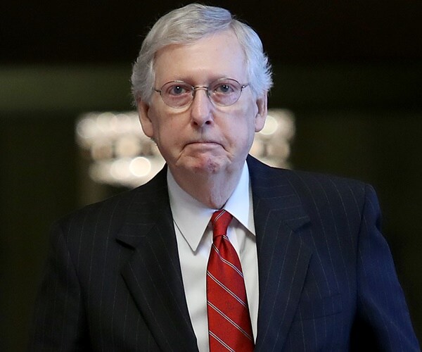 mitch mcconnell walks to camera against a dark backgroun