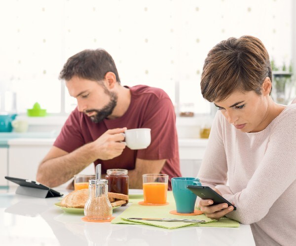 a couple in their kitchen looking at cell phones instead of talking to each other