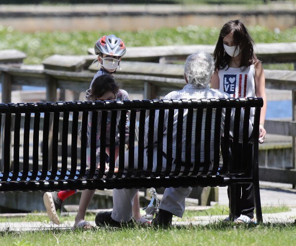 children talking to an elderly man in the park while wearing face masks