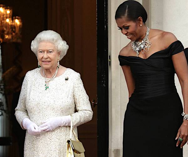 queen elizabeth ii smiles dressed in white and michelle obama, dressed in black, looks down on the queen's left