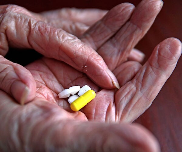 an ederly woman holds yellow and white statin pills in her right palm