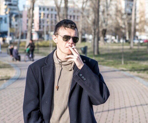 man smoking while walking through park