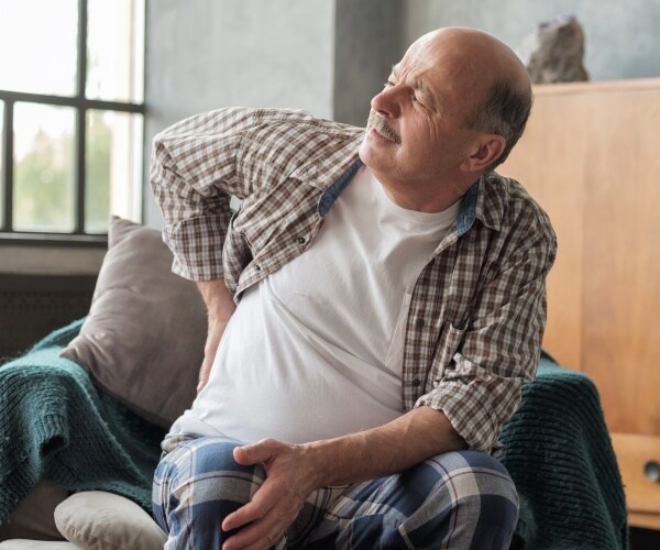 man sitting in chair with his hand at his back, having pain in kidney from kidney stones